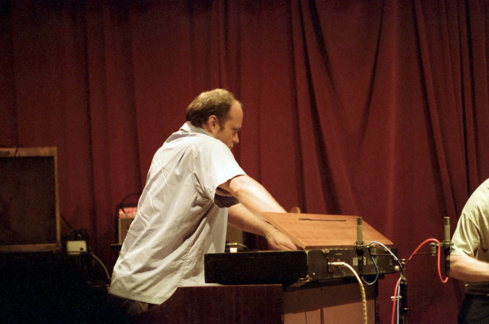 A keyboardist in a pale shirt leans over a clavinet wired with microphones.